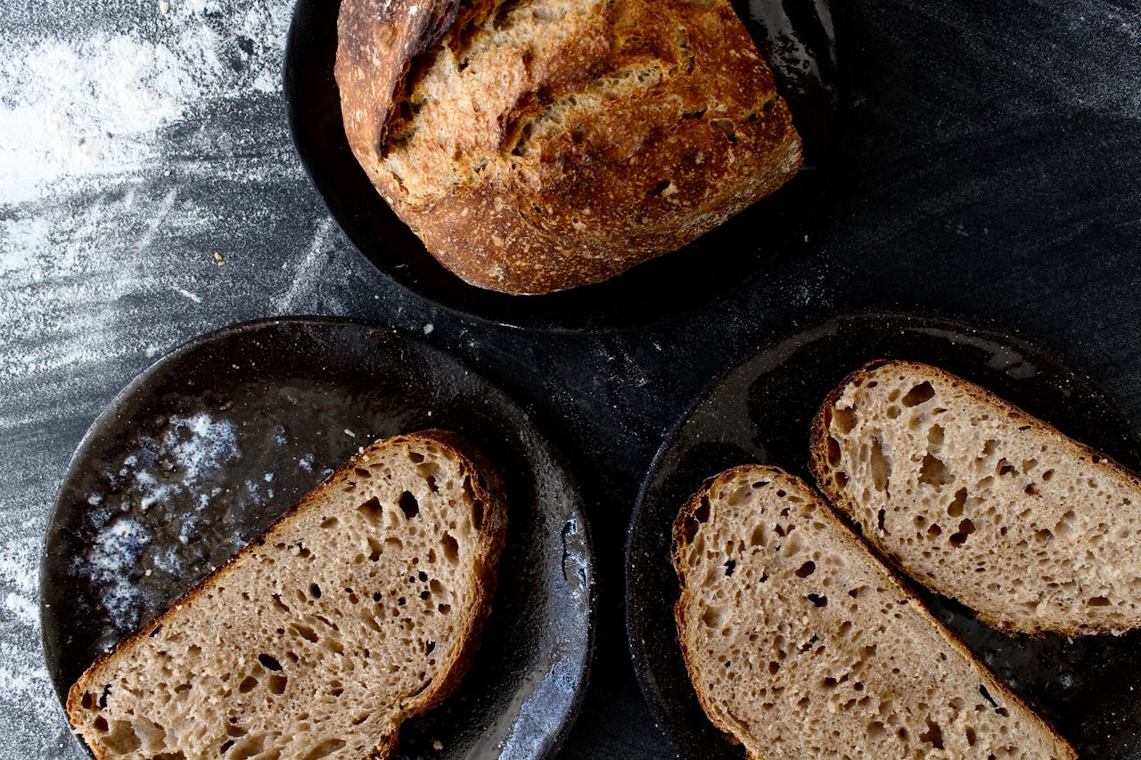 Home Freshly baked sourdough loaf and slices on dark plates with flour dusted surface.