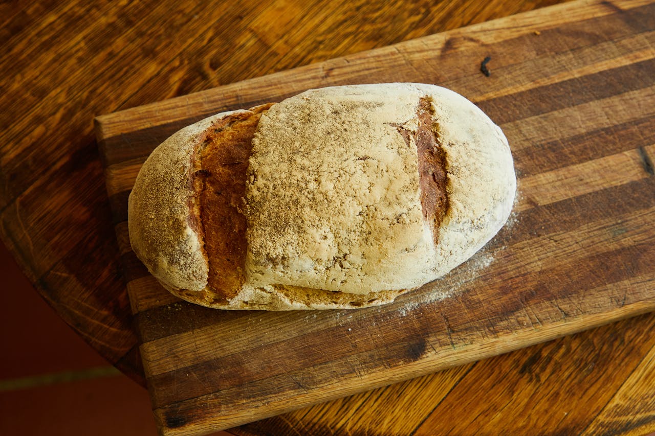 A freshly baked rustic loaf of bread on a wooden cutting board, ideal for culinary content.