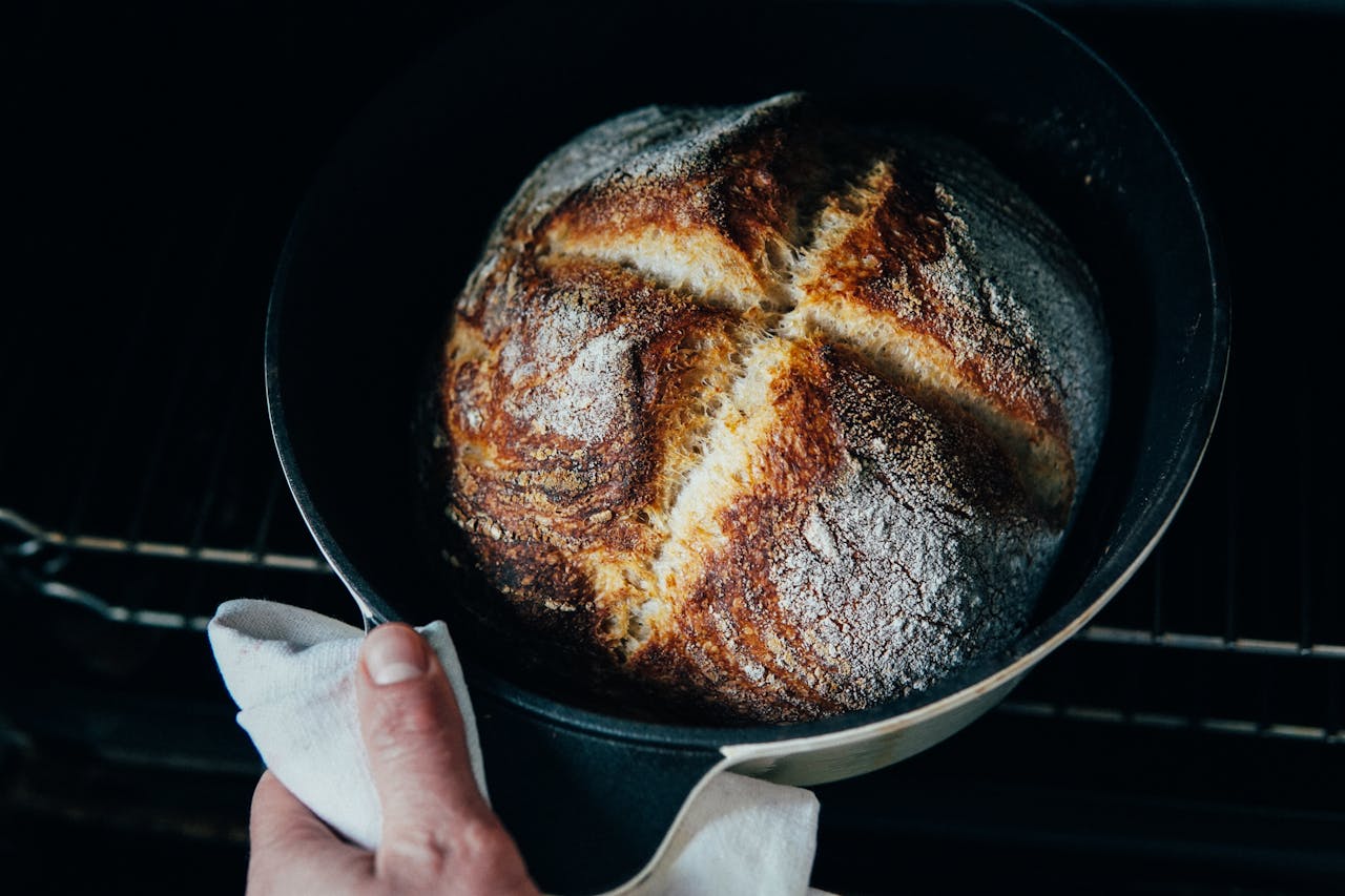 Home From above of crop anonymous chef pulling out fresh crispy bread from oven
